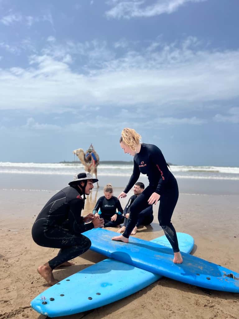IKO surf instructor teaching stance on the beach in Essaouira, Morocco, with students watching and the Atlantic in the background