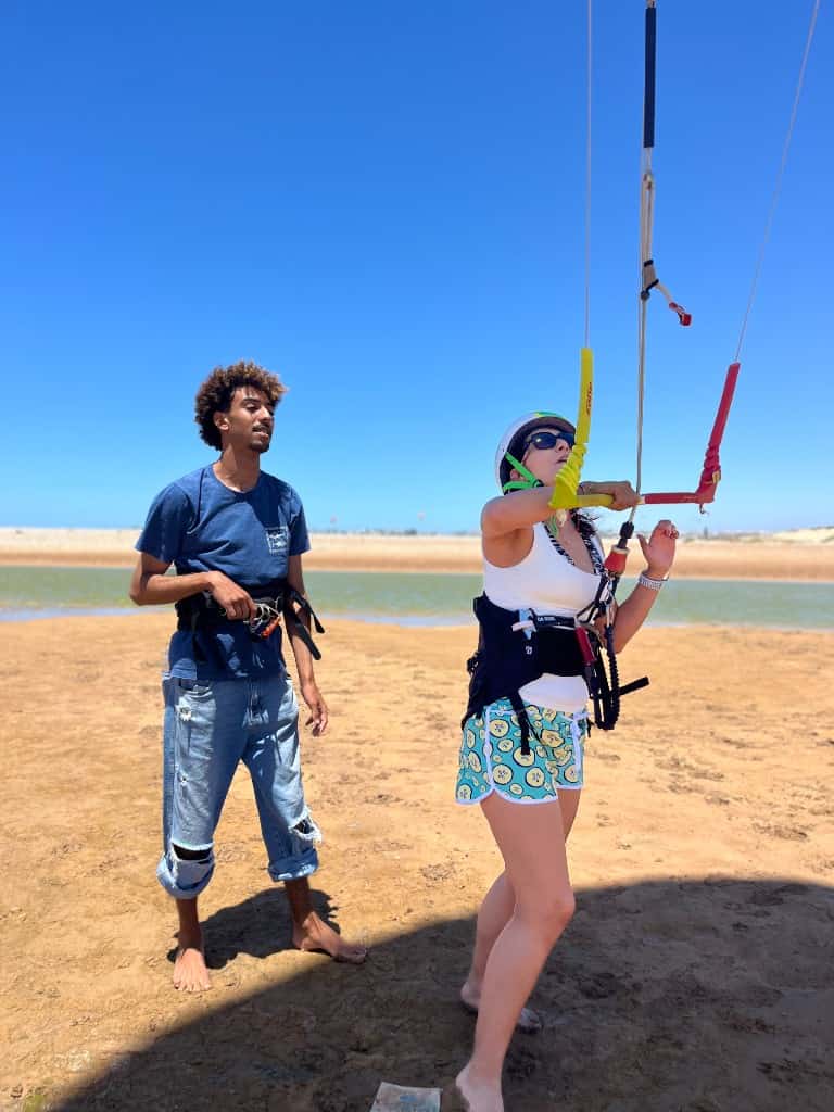 Kitesurfer in a helmet preparing a yellow kite on Essaouira beach with camels in the background