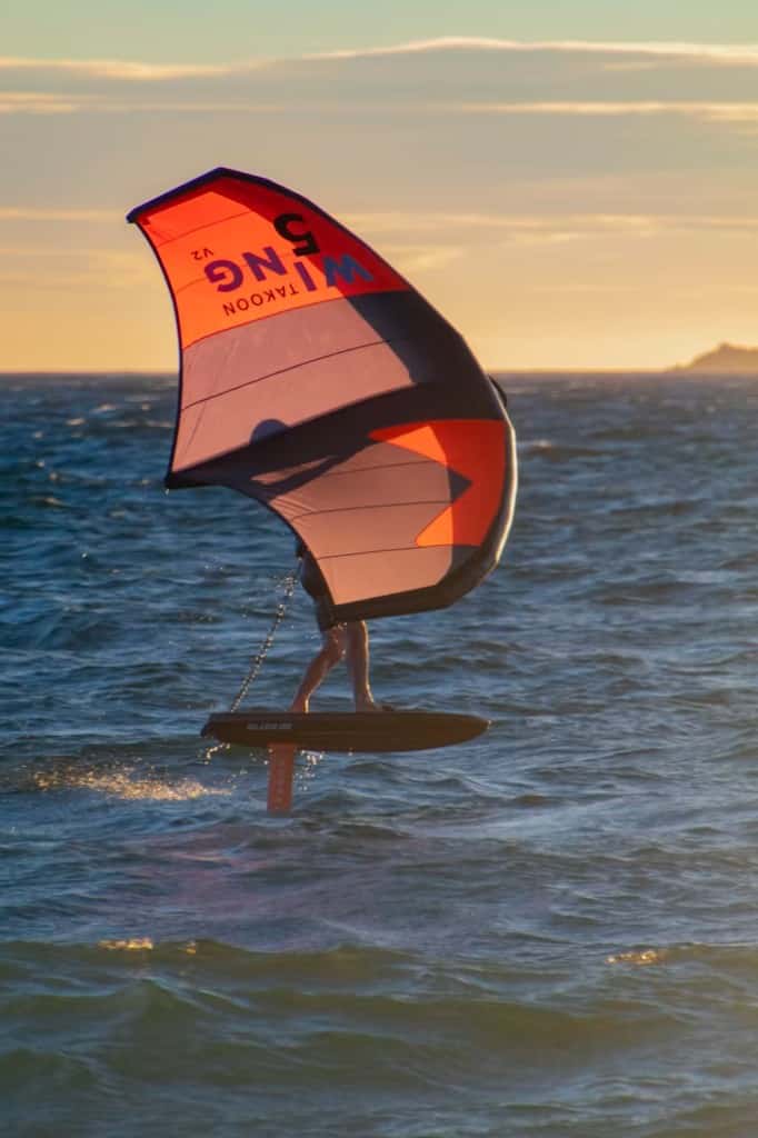 Wingfoiler on a teal foil board holding a wing sail above the water at Essaouira